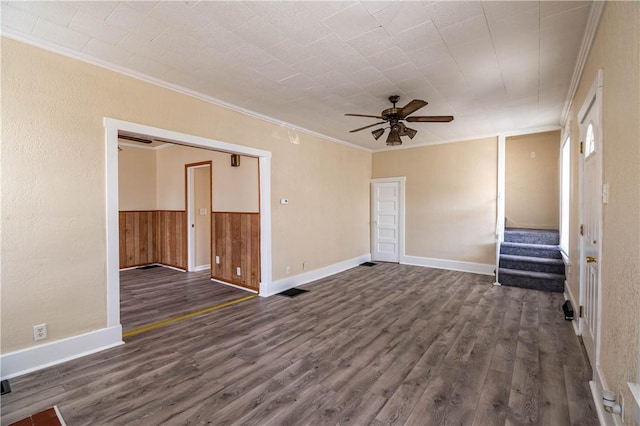 empty room featuring baseboards, stairs, ornamental molding, a ceiling fan, and dark wood-style flooring