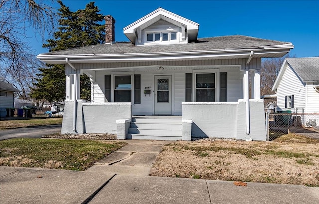 bungalow with a shingled roof, fence, covered porch, and a chimney