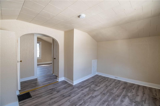 additional living space featuring visible vents, baseboards, lofted ceiling, arched walkways, and dark wood-style flooring