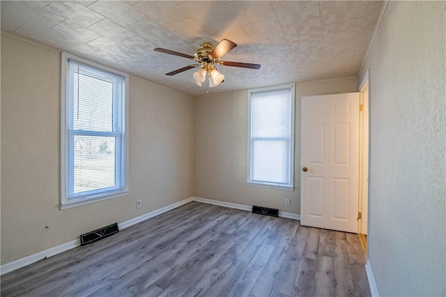 empty room with visible vents, a healthy amount of sunlight, baseboards, and wood finished floors