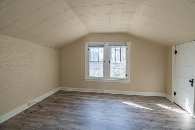 additional living space with baseboards, wood finished floors, and vaulted ceiling