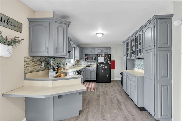 kitchen featuring light wood finished floors, stainless steel microwave, freestanding refrigerator, a peninsula, and gray cabinetry