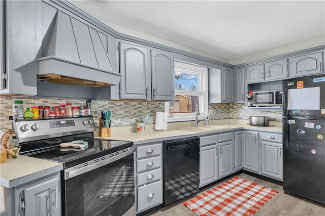 kitchen with premium range hood, a sink, light wood-style floors, gray cabinets, and black appliances