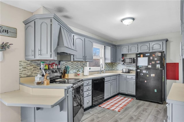 kitchen featuring gray cabinetry, a sink, light wood-style floors, black appliances, and custom range hood