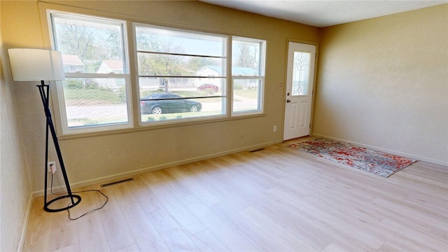 interior space with baseboards, a textured wall, wood finished floors, and visible vents