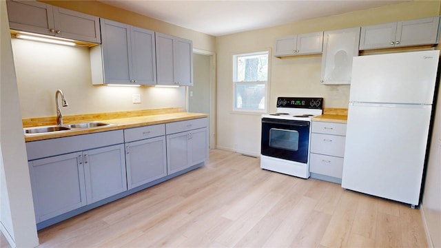 kitchen with gray cabinets, range with electric stovetop, a sink, freestanding refrigerator, and light wood-style floors