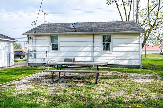rear view of property featuring a yard, a shingled roof, and fence