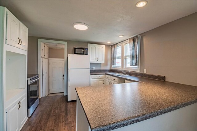 kitchen featuring dark wood finished floors, stainless steel range with electric cooktop, dark countertops, freestanding refrigerator, and a peninsula