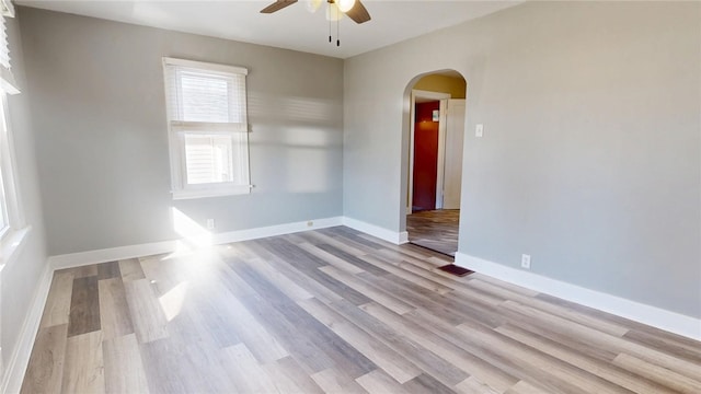 empty room with arched walkways, baseboards, a ceiling fan, and wood finished floors