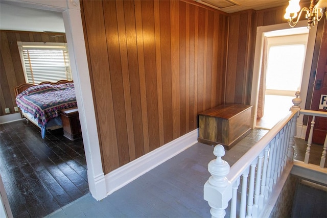 corridor featuring wooden walls, dark hardwood / wood-style floors, and an inviting chandelier