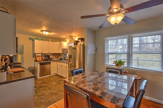 kitchen featuring ceiling fan, appliances with stainless steel finishes, dark stone countertops, hardwood / wood-style floors, and white cabinets