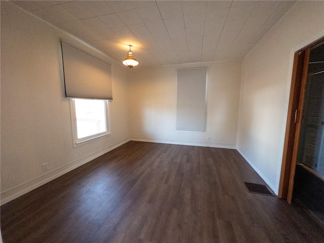 spare room featuring dark wood-style floors, visible vents, and baseboards