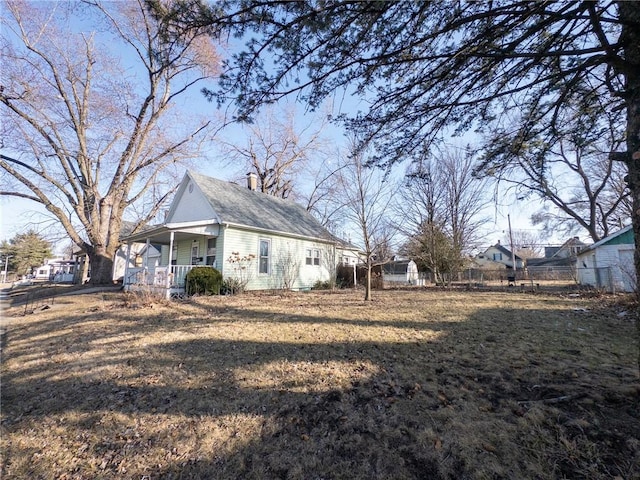 view of side of home featuring a lawn, a porch, a chimney, and fence