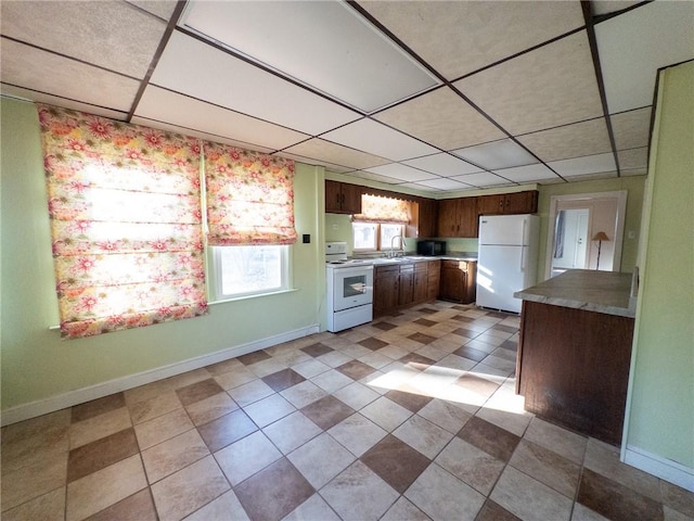 kitchen with a drop ceiling, white appliances, baseboards, and a sink