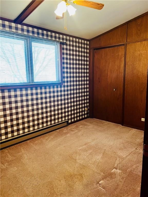 unfurnished bedroom featuring wallpapered walls, ceiling fan, carpet floors, a baseboard heating unit, and a closet