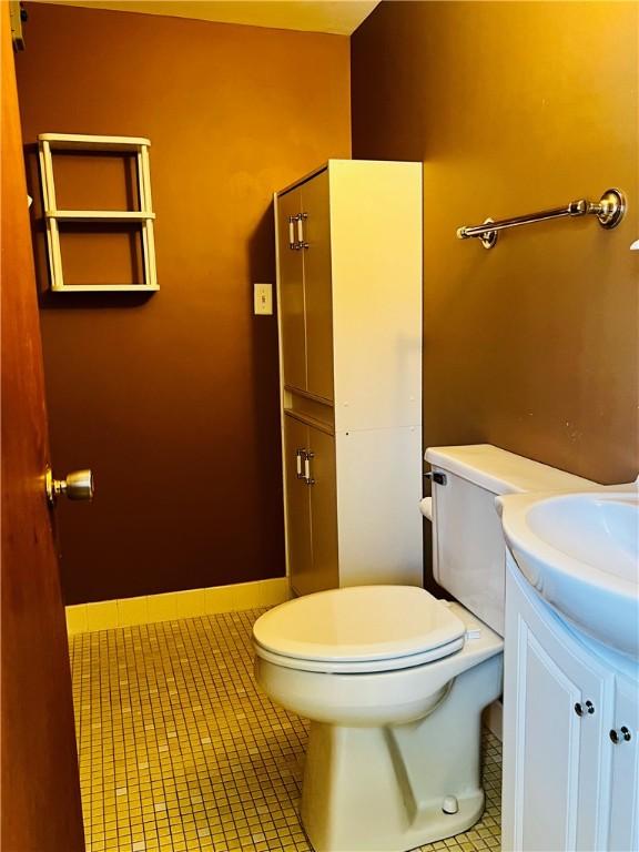 half bath with baseboards, vanity, toilet, and tile patterned floors