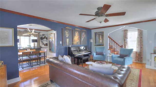 living area with crown molding, arched walkways, wood finished floors, stairway, and ceiling fan with notable chandelier