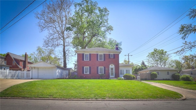 colonial home with a garage, a front lawn, fence, a chimney, and an outbuilding