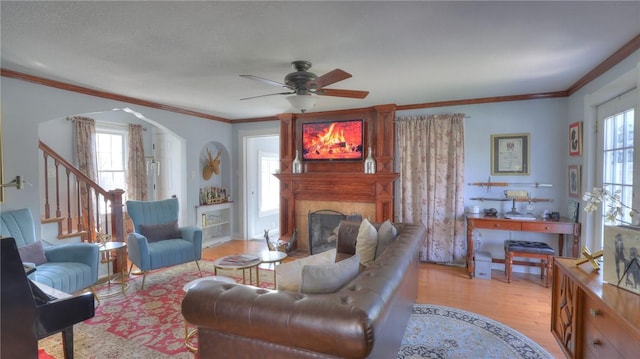 living area featuring ceiling fan, a fireplace, arched walkways, wood finished floors, and ornamental molding