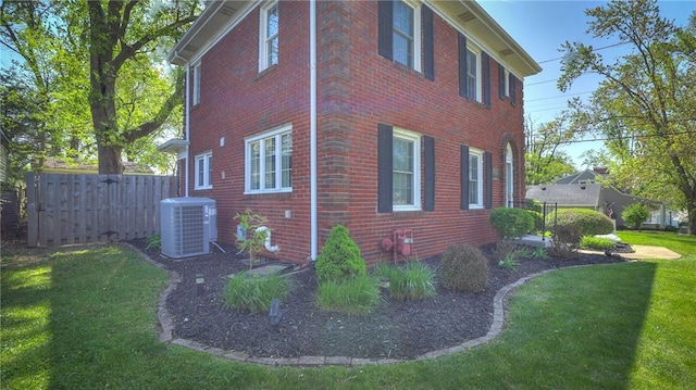 view of side of property featuring fence, central AC unit, a yard, and brick siding