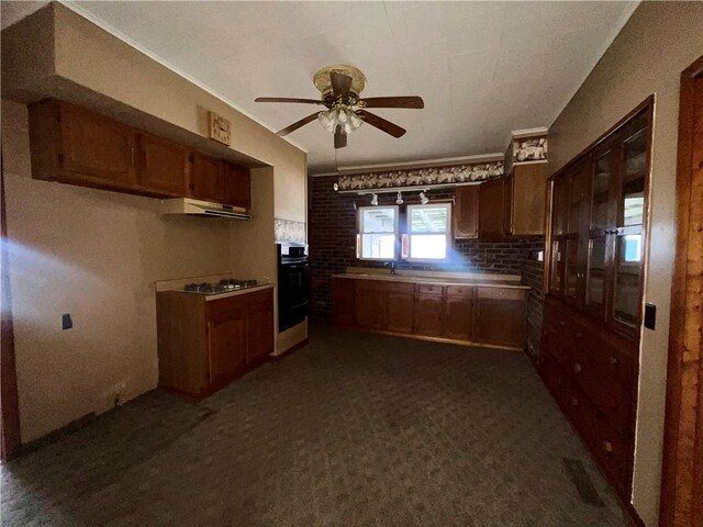 kitchen featuring dark colored carpet, oven, sink, ceiling fan, and gas stovetop