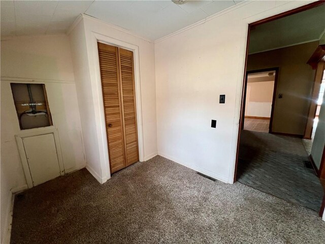 unfurnished bedroom with dark colored carpet, a closet, and crown molding