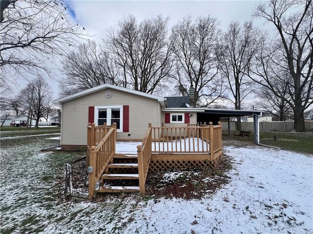 snow covered rear of property featuring a deck and a carport