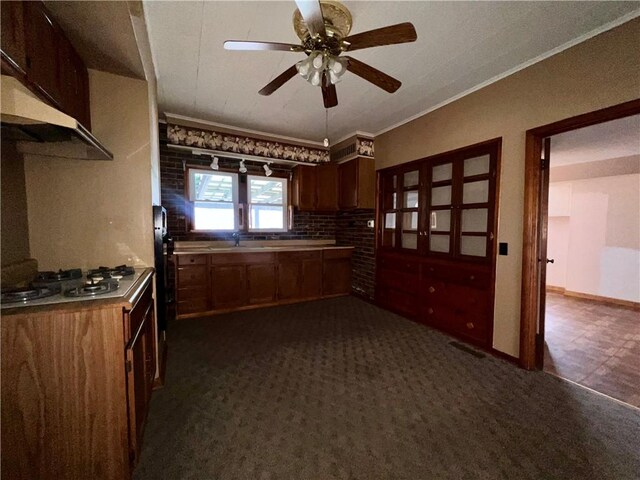 kitchen featuring dark carpet, ceiling fan, ornamental molding, and stainless steel gas cooktop