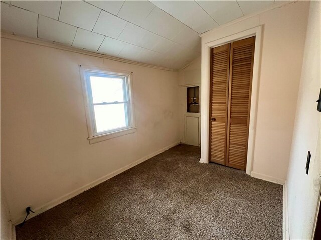 unfurnished bedroom featuring carpet, lofted ceiling, ornamental molding, and a closet