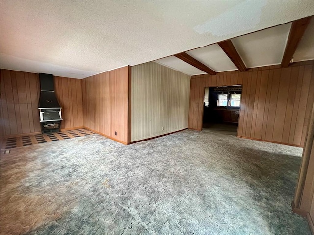 unfurnished living room with carpet flooring, wooden walls, beamed ceiling, and a textured ceiling