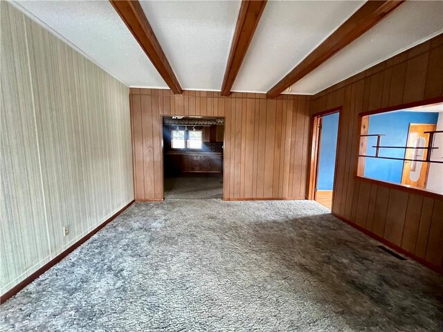 unfurnished living room featuring wooden walls, beamed ceiling, and light carpet