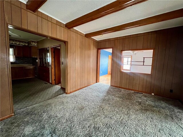 unfurnished room with wooden walls, carpet flooring, a textured ceiling, beam ceiling, and a chandelier