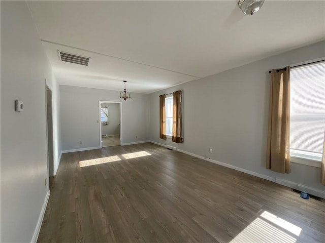 unfurnished room with a healthy amount of sunlight, dark hardwood / wood-style floors, and an inviting chandelier