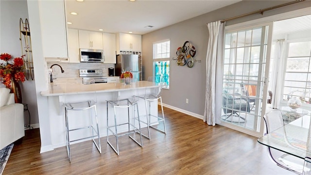 kitchen with appliances with stainless steel finishes, tasteful backsplash, wood finished floors, baseboards, and a breakfast bar