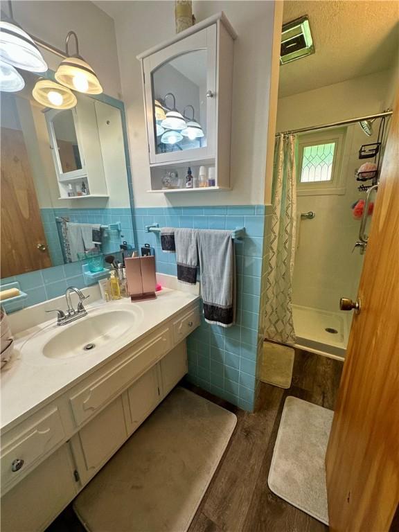 1712 Southdale Dr, Mattoon, IL 61938 - bathroom with tile walls, a tile shower, wood finished floors, vanity, and a wainscoted wall