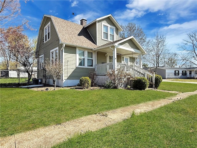 bungalow-style house featuring a front yard, central AC, fence, a shingled roof, and covered porch