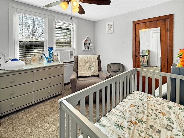 bedroom with a crib, a textured ceiling, a ceiling fan, cooling unit, and carpet