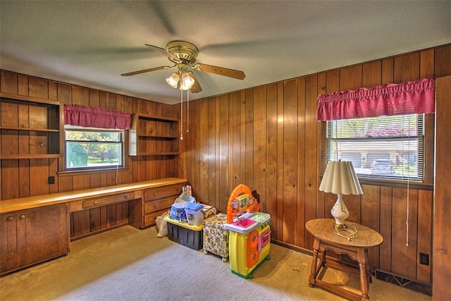 rec room featuring wood walls, carpet, built in desk, and ceiling fan