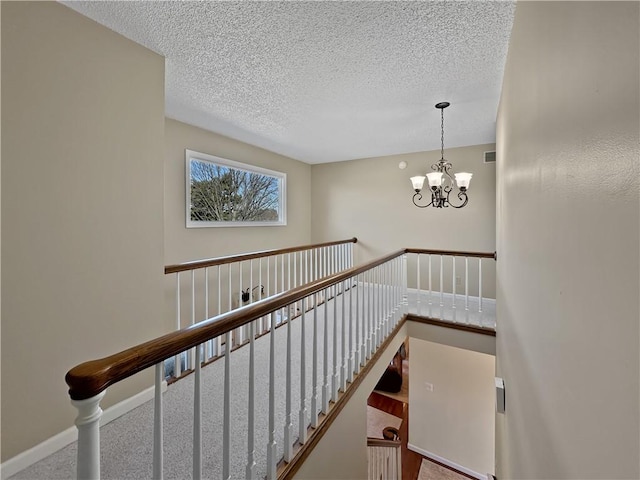 stairs with baseboards, a notable chandelier, carpet floors, and a textured ceiling