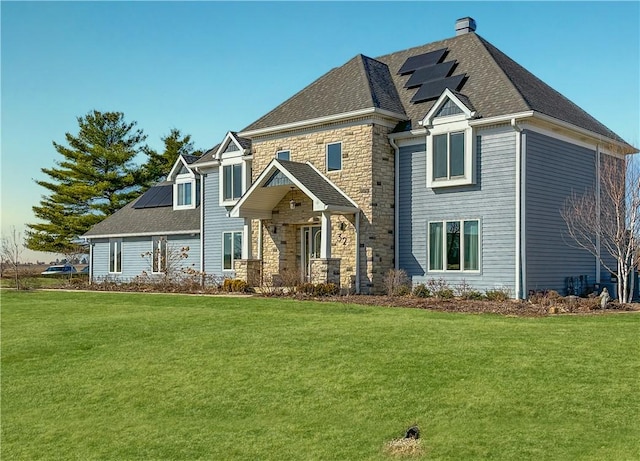 view of front facade featuring stone siding, solar panels, a front yard, and roof with shingles