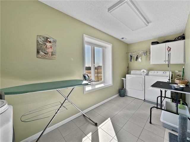 washroom featuring light tile patterned floors, baseboards, cabinet space, a textured ceiling, and washer and clothes dryer