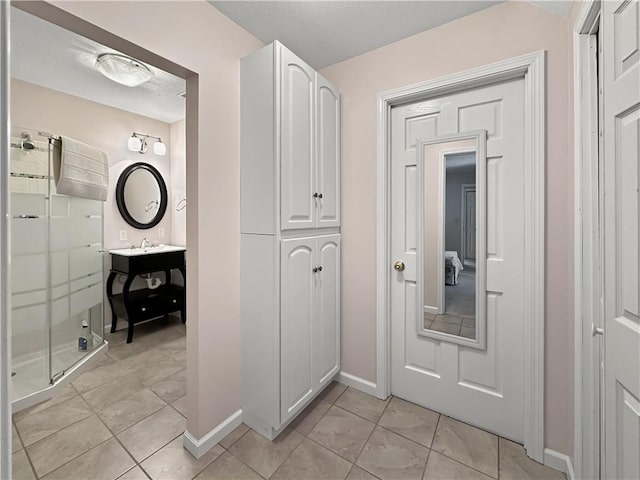 corridor featuring light tile patterned floors, baseboards, and a sink