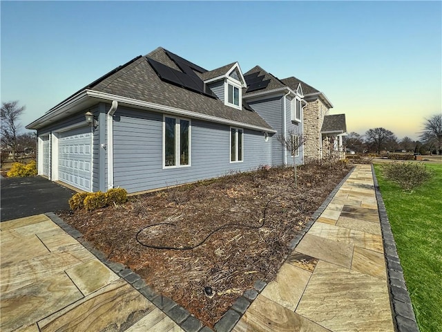 view of property exterior with solar panels, driveway, a shingled roof, and a garage