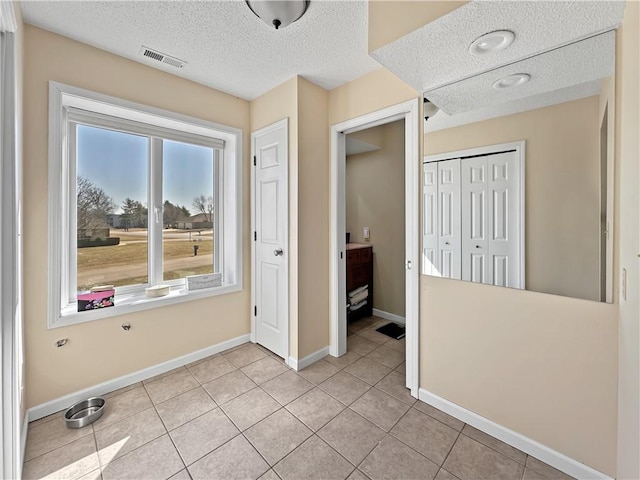 interior space with visible vents, a textured ceiling, a closet, light tile patterned floors, and baseboards