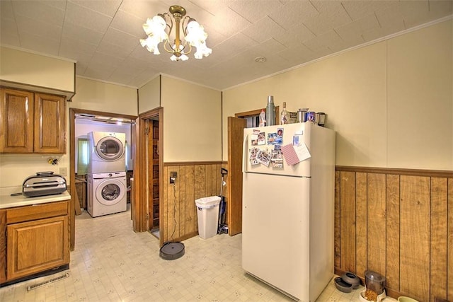 1212 Washington St, Clinton, IL 61727 - kitchen featuring freestanding refrigerator, stacked washing machine and dryer, brown cabinets, a chandelier, and wood walls