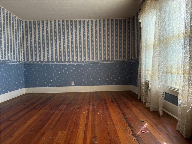 unfurnished room with baseboards, wallpapered walls, and hardwood / wood-style floors
