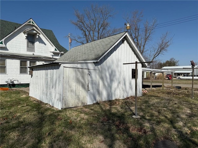 view of property exterior featuring a shingled roof, an outdoor structure, and a yard