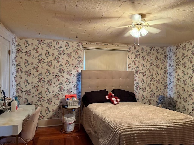bedroom featuring baseboards, wallpapered walls, wood finished floors, and a ceiling fan