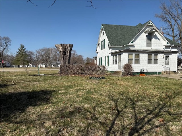 view of side of home featuring roof with shingles, entry steps, and a yard
