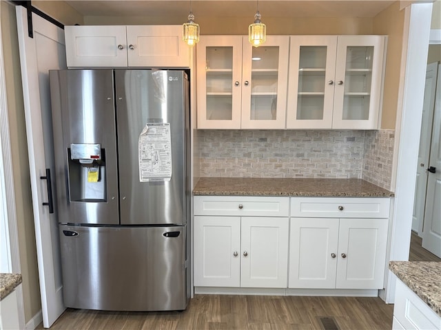 kitchen with backsplash, stainless steel refrigerator with ice dispenser, light stone countertops, white cabinets, and decorative light fixtures